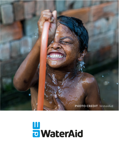 A laughing young boy sprays himself with water from a garden hose while playing outside.