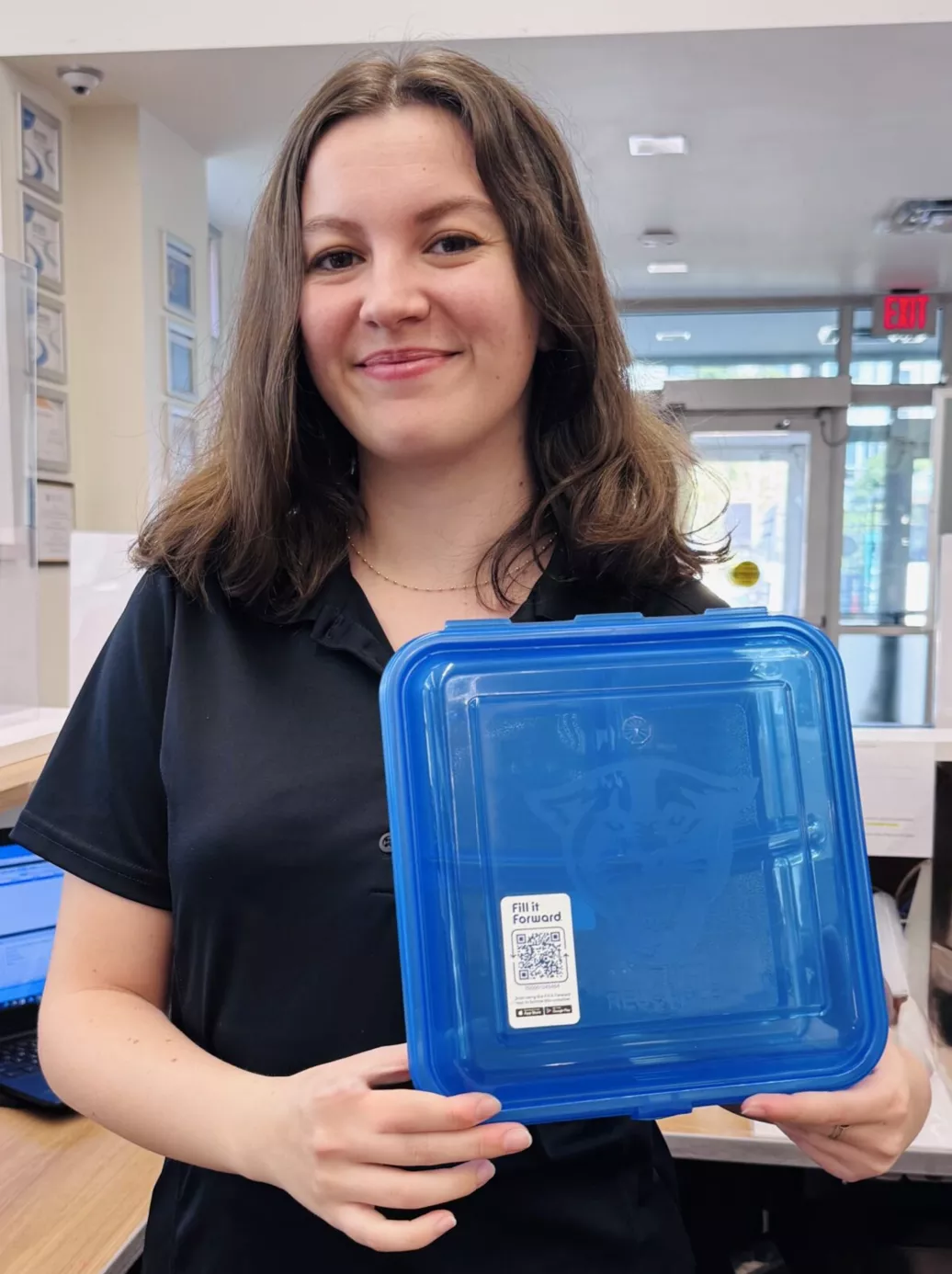 woman holding reusable container with fill it forward sticker on it