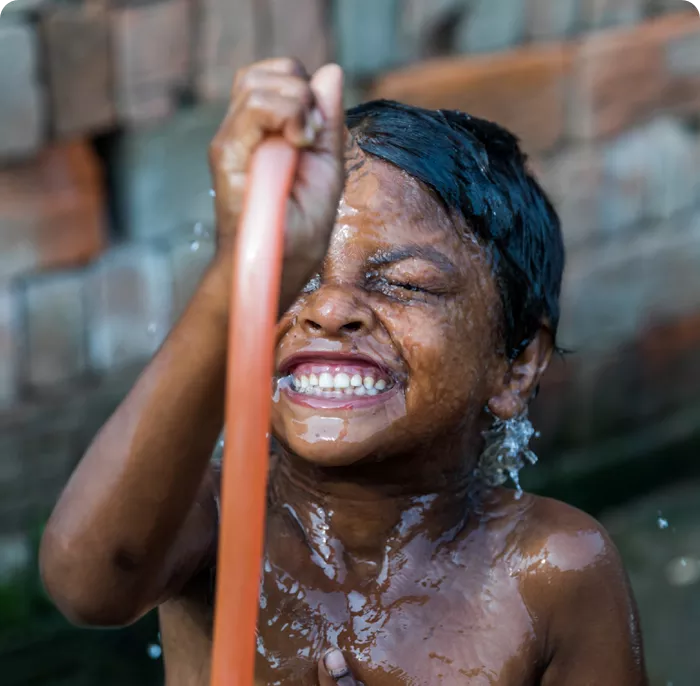 A laughing young boy sprays himself with water from a garden hose while playing outside.